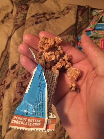 A reviewer holding an opened pack of the granola bar 