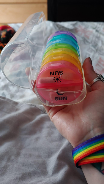 reviewer holding clear case with rainbow round smaller cases for each day of the week