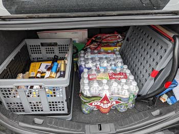 Trunk of a car packed with groceries including water bottles and household items for shopping needs