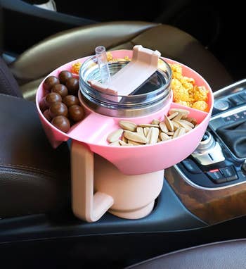 the pink bowl sitting in a car cup holder, holding various snacks