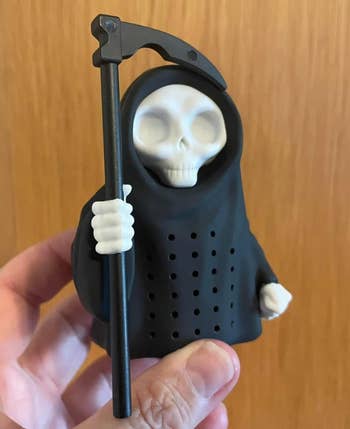 Hand holding a tiny Grim Reaper figurine with a scythe, designed arsenic a beverage infuser
