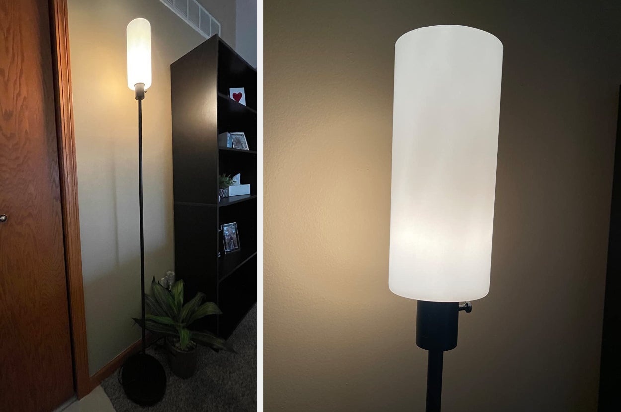 Reviewer image of tall skinny black lamp with cylinder milky white light post, close up of product turned on in front of a white wall
