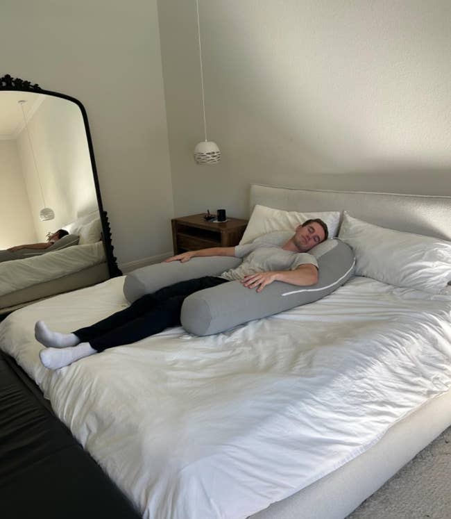 Person sleeping comfortably on a large supportive body pillow, lying on a neatly made bed in a minimalist bedroom setting
