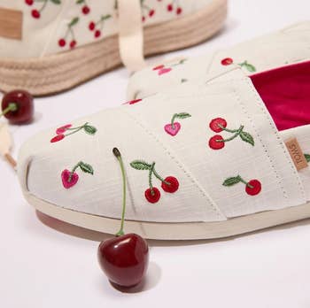 Close-up of shoes with embroidered cherries and espadrille soles, alongside a caller cherry. Retro summertime footwear style