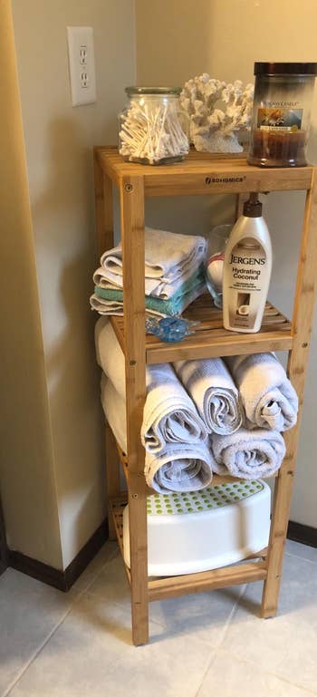Reviewer image of bamboo four-tier standing shelf in the corner of a room with towels and bottles on each surface