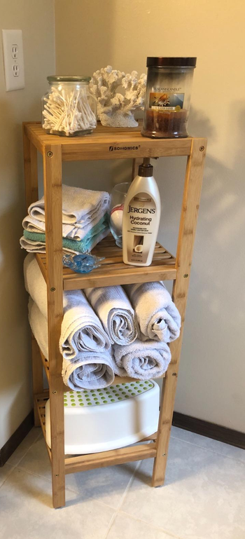 Reviewer image of bamboo four-tier standing shelf in the corner of a room with towels and bottles on each surface