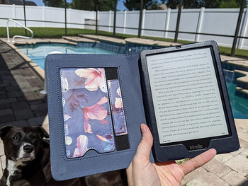 Reviewer holding the Kindle  Paperwhite by the pool with their dog alongside them