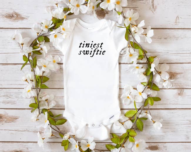 white baby onesie with black text on it that reads 