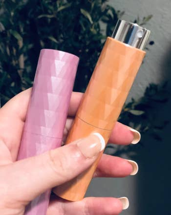a reviewer holding the shiny pink and orange spray bottles which are roughly the size of a mascara tube