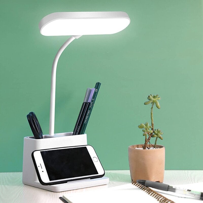 lifestyle image of a white lamp on a desk with pen holder and phone holder