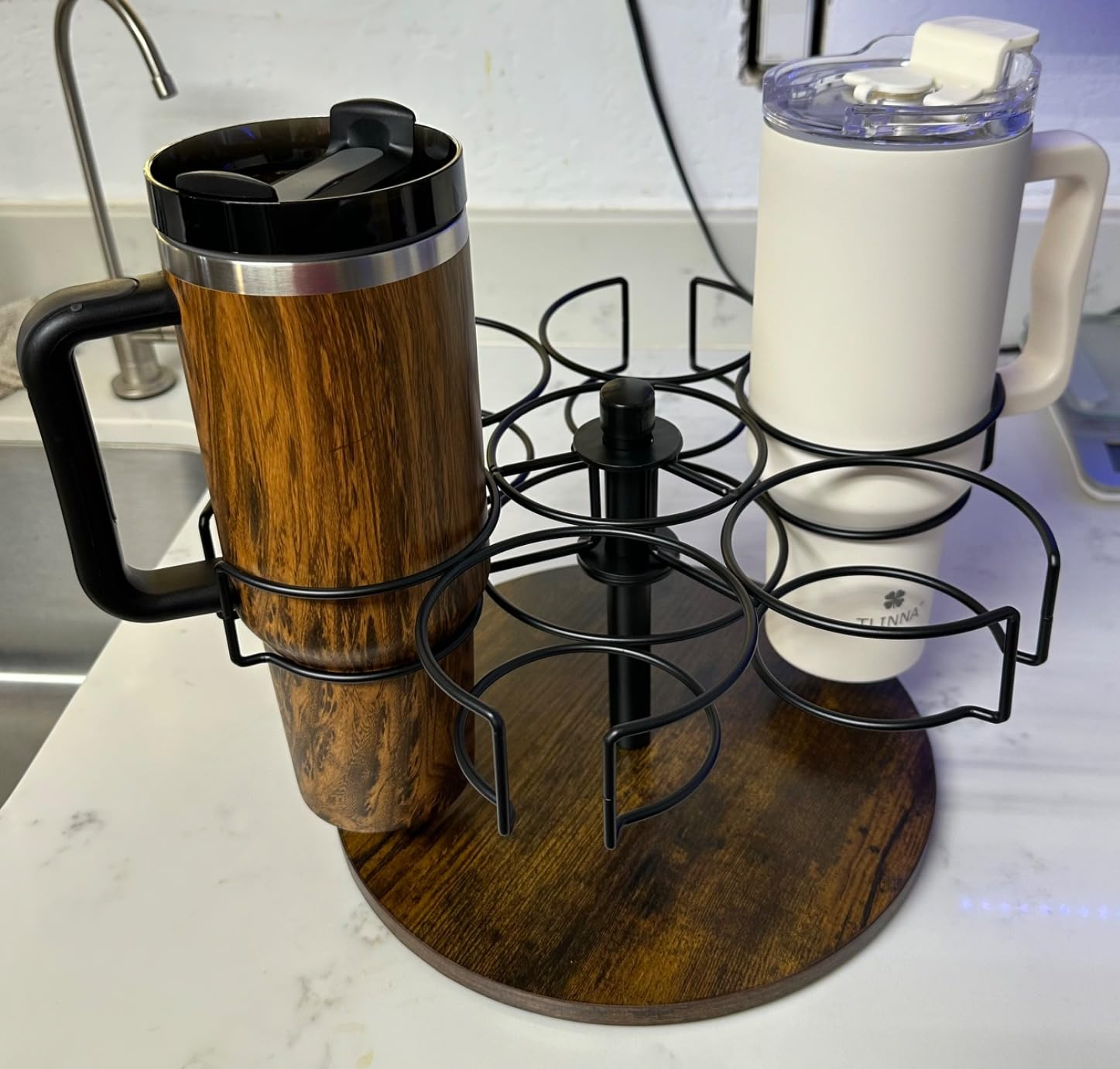 Two travel mugs, wood-patterned and white, placed on a rotating rack in a kitchen setting. The rack can hold up to six mugs and is on a marble countertop