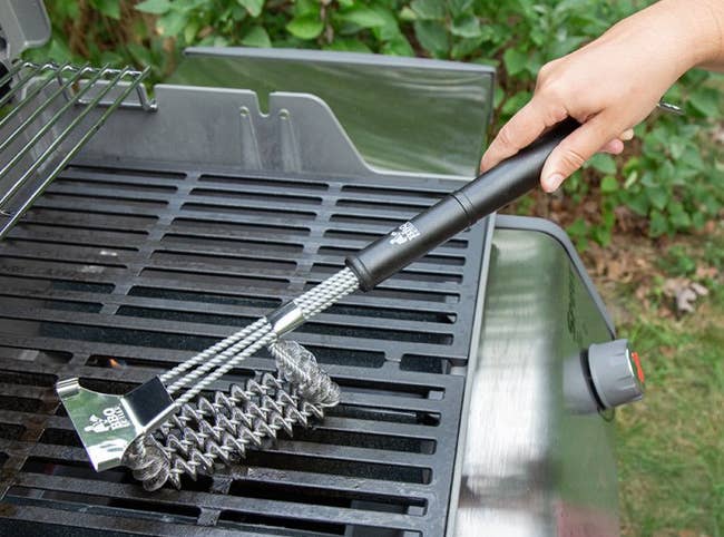 a model using the grill brush to clean an outdoor grill grate 