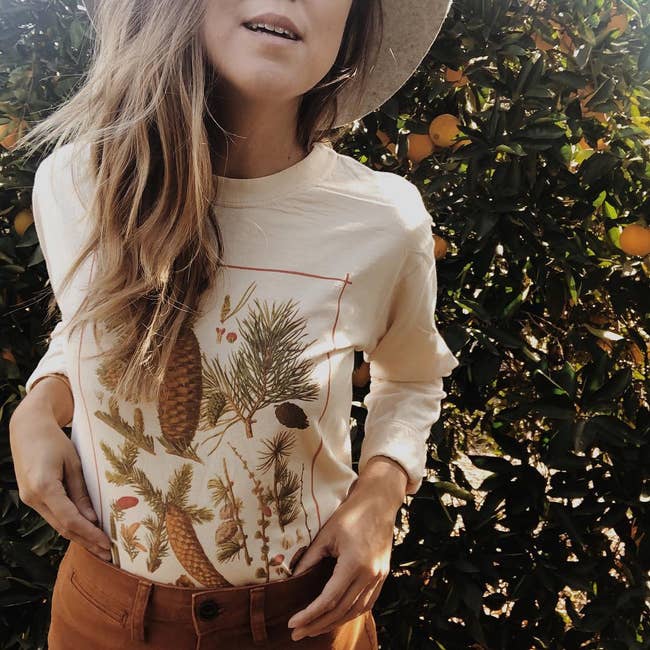 a model in a tan long sleeve with a vintage styled print of pine needles on it