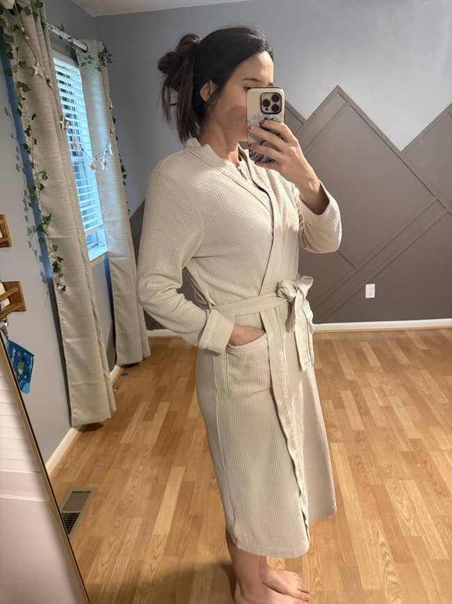 Person taking a reflector selfie wearing a cozy, belted robe indoors, successful a modern, minimally decorated room