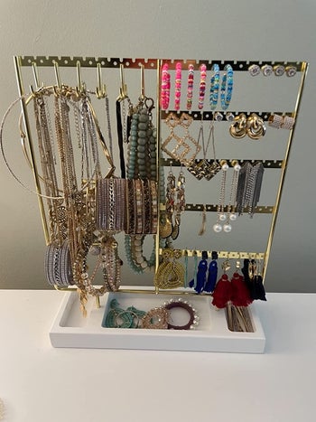 Reviewer image of gold and white  jewelry organizer with earrings and necklaces hanging on hooks