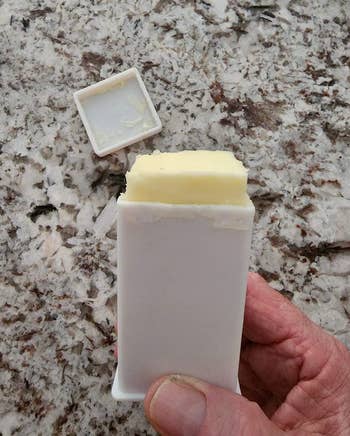 A reviewer holding a white dispenser with a stick of butter inside it 