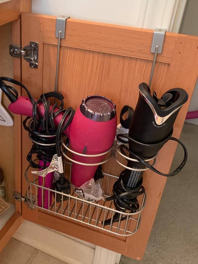 reviewer's  over-the-door organizer hanging on a bathroom cabinet door holding styling tools