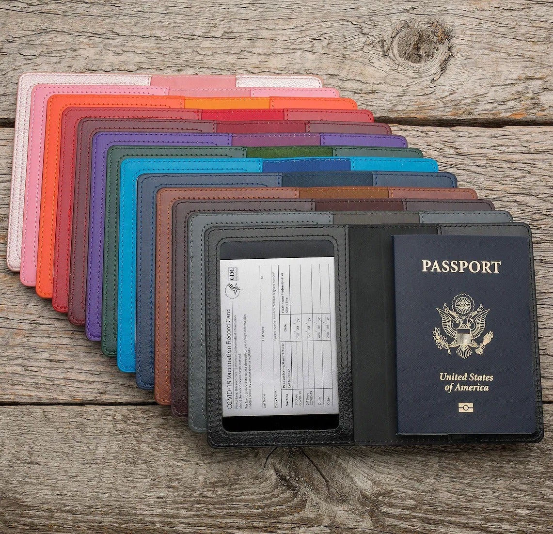a stack of passport holders in assorted colors, with the one in front opened and holding a vaccination card and passport