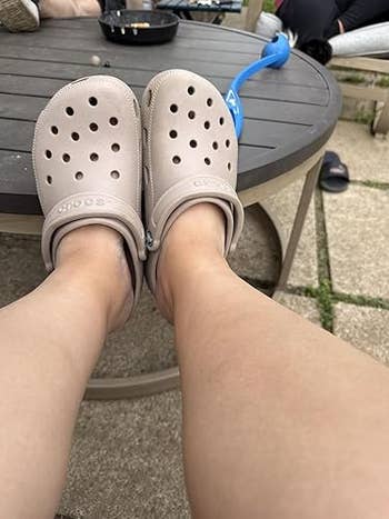 Person wearing Crocs, seated connected a patio with a circular array successful the background. Relaxed outdoor setting, highlighting casual footwear