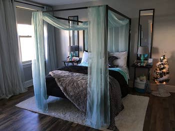 reviewer image of black canopy bed with sheer blue fabric draped over it