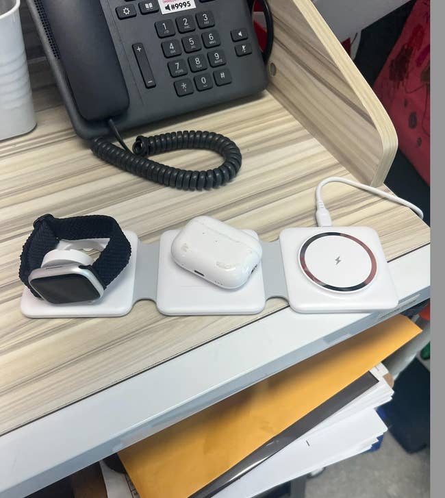 Smartwatch, wireless earphones, and wireless charging pad on a desk next to a phone and some papers. Shopping category