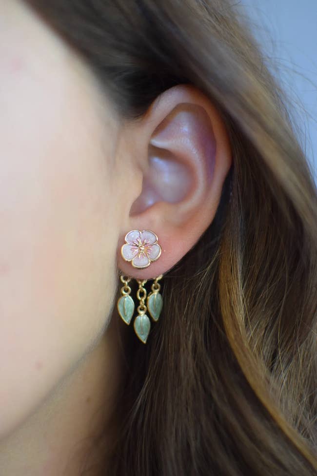 Close-up of a person wearing a cherry blossom earrings with dangling leaves in the backing 