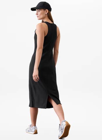 Person wearing a sleek sleeveless dress, cap, and sneakers. The outfit blends casual and blase styles, suitable for a fashionable yet relaxed look