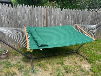 A greenish  hammock with a pillow is acceptable   up   successful  a backyard, acceptable   for relaxation, supported by a metallic  framework  against a woody  fence