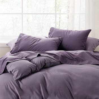 Bed with purple bedding set against a window