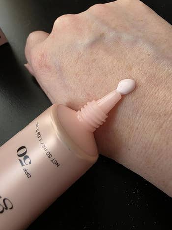 A close-up of a manus  with airy  skin, applying pinkish  SPF 50 sunscreen from a tube