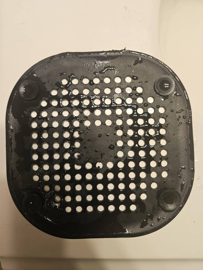 Black perforated rubber sink drain cover with water droplets