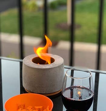 reviewer photo of the portable fireplace on an outdoor table next to a glass of wine and bowl of snacks