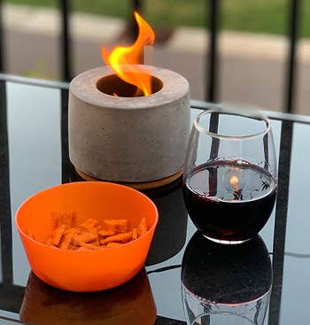 reviewer photo of the portable fireplace on an outdoor table next to a glass of wine and bowl of snacks
