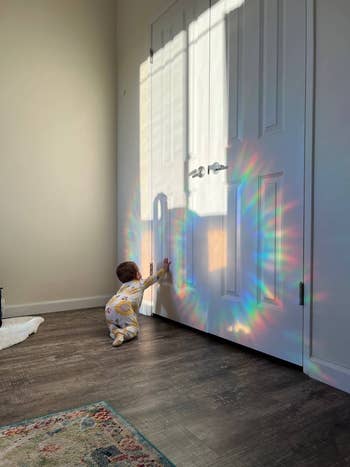 Toddler reaching for light patterns on a door from a prism, wearing a patterned outfit