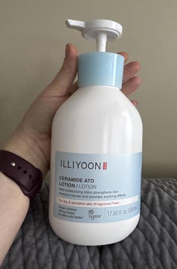 Person holding a vessel of Illiyoon Ceramide Ato Lotion, labeled for adust and delicate skin, connected a textured surface