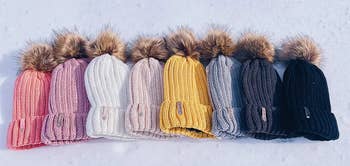 eight beanies with pom poms lined up on the snow