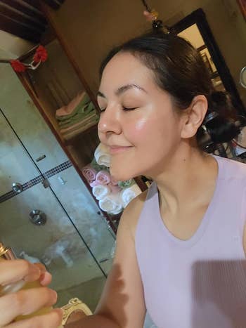 Person successful  a bath  utilizing a facial spray, wearing a sleeveless top, surrounded by rolled towels and a ablution  successful  the background