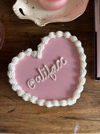 Fake cake box with white icing and pink frosting design that says BuzzFeed writer Ali Faccenda's name