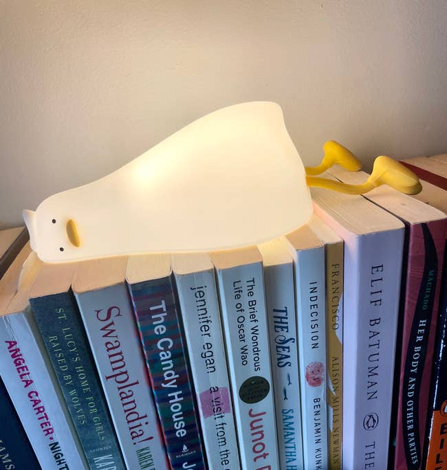Books arranged on a shelf with a small polar bear-shaped nightlight on top and a pair of yellow glasses beside it. A mini