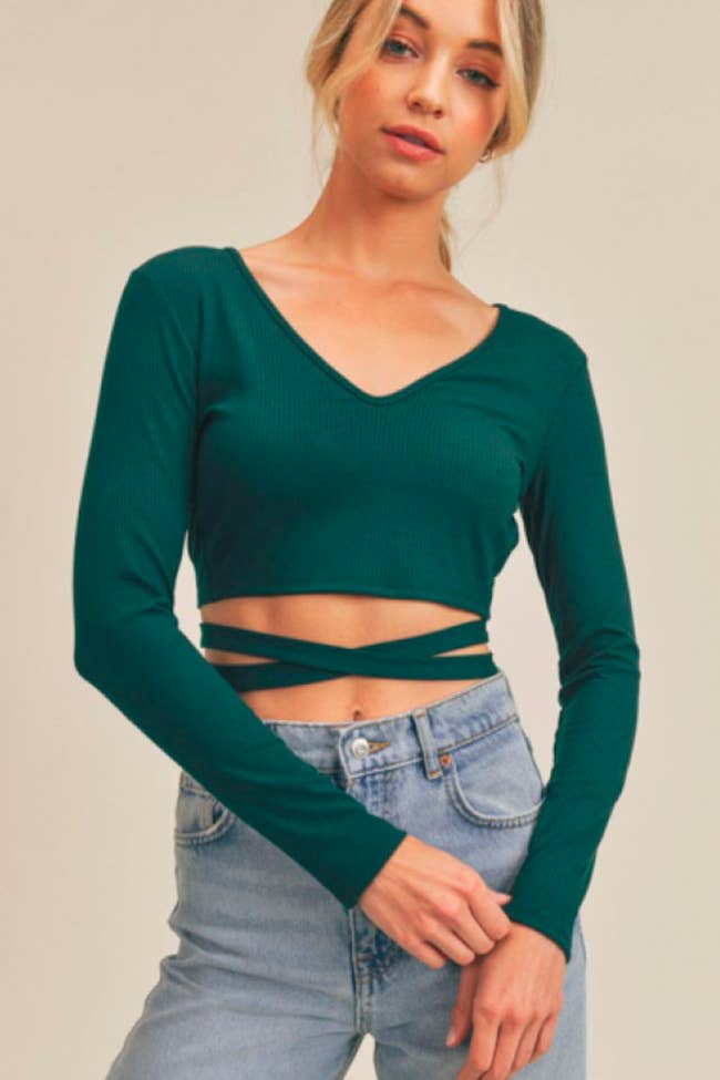 model wearing cropped long-sleeved shirt in dark green with criss cross straps across stomach