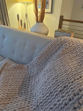 another reviewer's sandstone chunky blanket draped over a couch in a stylish living room setting