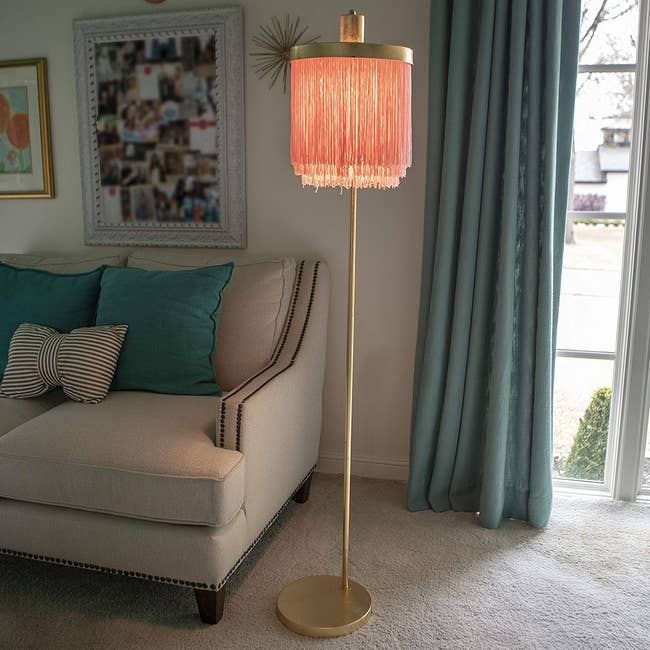 living room with gold tone floor lamp that has a pink fringe shade on it 