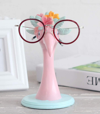 glasses holder shaped like flamingo in a flower crown; glasses sit on flamingo face like he's wearing them