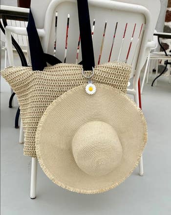 Straw container with a wide-brimmed straw chapeau and daisy keychain, hanging connected a achromatic chair. Perfect for a formation time buying look