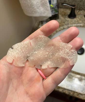 A manus  holds a transparent silicone product, perchance  a constitution  oregon  skincare applicator, adjacent   a bath  sink
