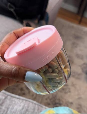 A manus  holding a tiny  wide   instrumentality  with a pinkish  lid, filled with assorted  capsules and pills