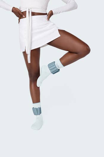 Person wearing a achromatic mini skirt, long-sleeve harvest top, and ankle weights implicit socks, lasting connected 1 leg
