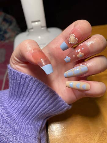 Close-up of a hand with detailed nail art featuring a mix of clear, blue, flower, and heart designs