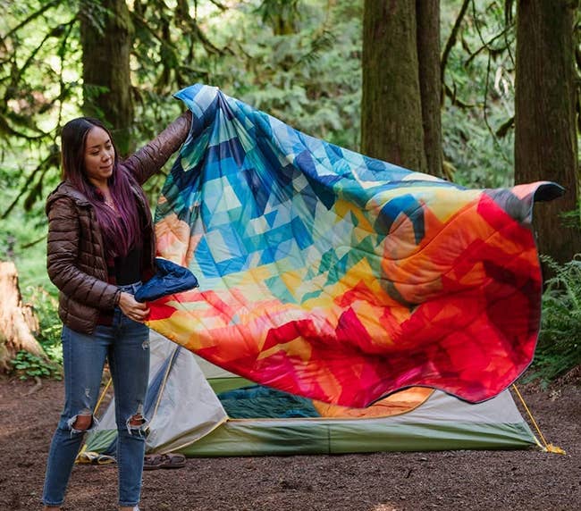 a model spreading out a quilted blanket with a rainbow print 
