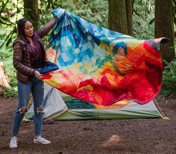 a model spreading out a quilted blanket with a rainbow print 